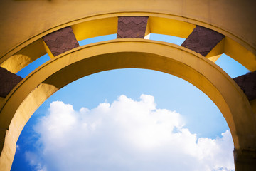 yellow arch against a blue sky with a cloud