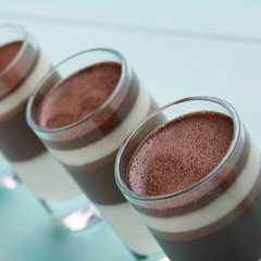 a lot of glasses with chocolate dessert stand in a row, on a turquoise background, the concept of a holiday and dessert, macro photography