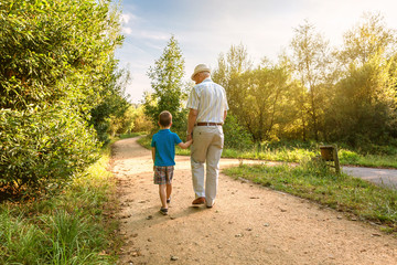 Back view of grandfather with hat and grandchild walking on a nature path - Powered by Adobe