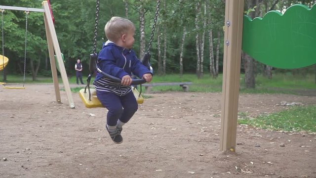 two year old boy is riding on a swing in the park