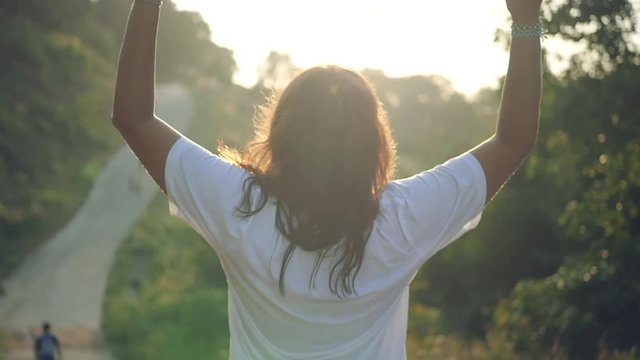 A young girl in a white T-shirt is standing with arms outstretched in the park at sunset. Slow motion, HD, 1920x1080