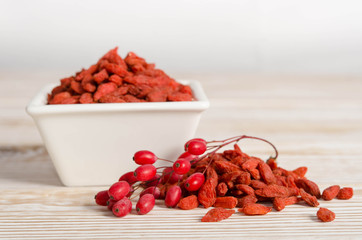 Branch of ripe red barberries and dried goji berries on wooden table