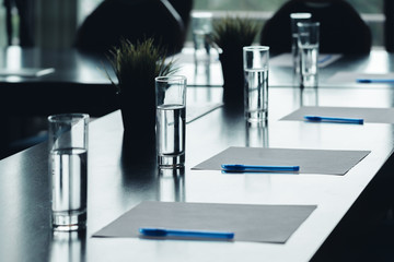 Close up of dark conference table water glasses pens, paper sheets