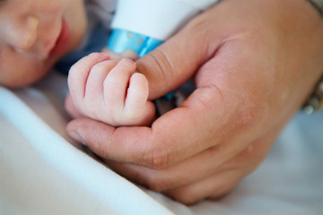 Big man's hand holding baby's hand.