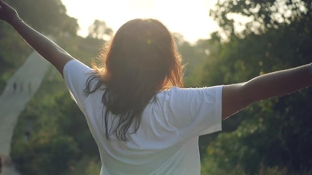 A beautiful girl stands in the park at sunset, arms outstretched, enjoying life. Slow motion, HD, 1920x1080