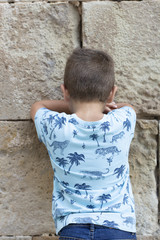 Little boy facing the wall outdoors at summer