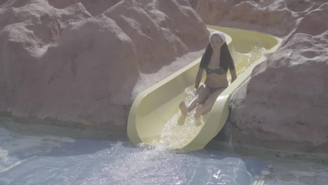 The girl is rolling fun with a water slide in the water park. A girl laughs and falls with a splash of water. S-log, ungraded