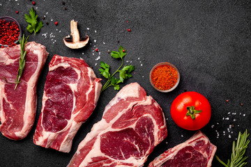 Meat raw steaks lie on a black background with vegetables, tomatoes, marasmade, mushrooms. background image. side view, copy space, top view