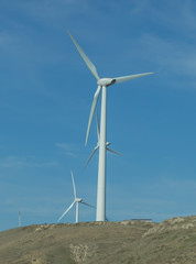 Wind farm: Industrial Eolic installation . Wind turbines towers again cloud blue sky on a wind farm sustainable, renewable energy concept. Alternative energy source from wind power.