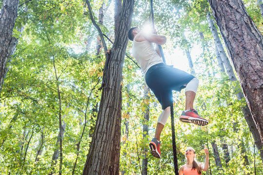 Man and woman climbing rope for sport in the woods cheering at each other