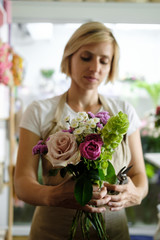 woman florist making bouquet of pink flowers indoor. Female florist preparing bouquet of roses in flower shop. entrepreneurship, small business, workplace concept 