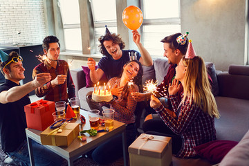 Friends with cake with candles celebrating birthday at a party in room.