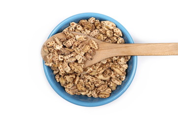 Organic barley flakes, pile in blue porcelain bowl with wooden spoon isolated on white background
