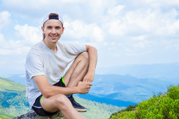 Naklejka na ściany i meble man hiker relaxing on top of hill and admiring beautiful mountain valley view in summer day