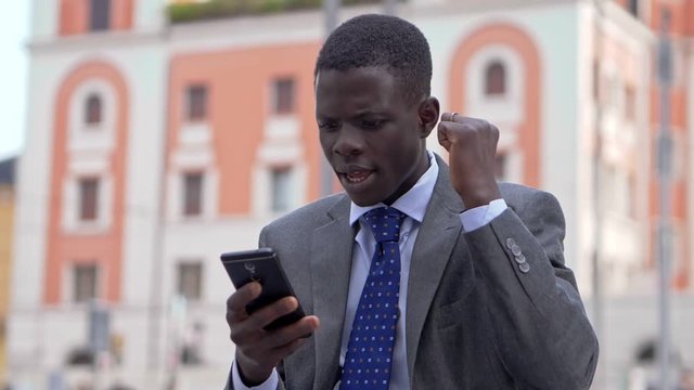 Young black african business man rejoicing looking at smartphone. Success,win