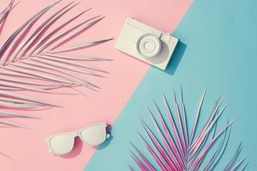 Beach accessories and palm leaves on pastel pink and blue background with copy space. Summer is coming concept. Minimal flat lay.