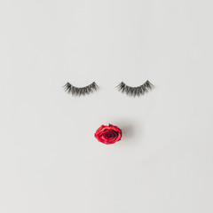 Creative woman face made of eyelashes and red rose flower lips. Minimal beauty concept. Flat lay.