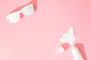 Creative layout with copy space, sunglasses and sunscreen or suntan lotion on pastel pink...
