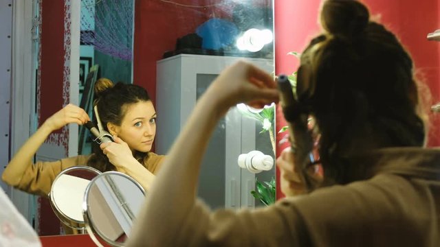 Young beautiful girl curls her hair on a curling robe in the dressing room, the artist prepares for a performance or photo shoot