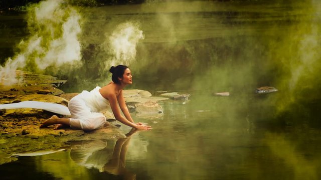 Beautiful girl sitting on the water. With smoke. She wears a white dress. Looking for something in the water. She looks very beautiful. Reflections mirror beautiful girl in the water. Concept art.