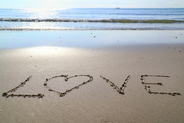 Text "LOVE" with the waves beat at the beach and sunlight in the summer morning.
