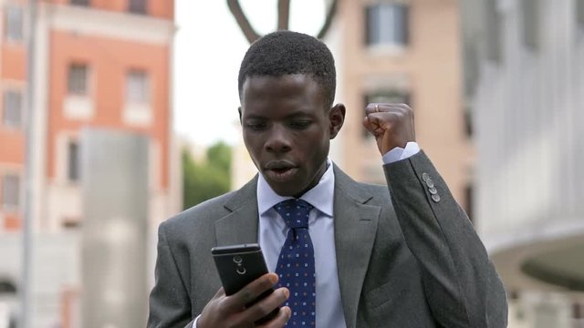 Young american african businessman typing on smartphone in the street