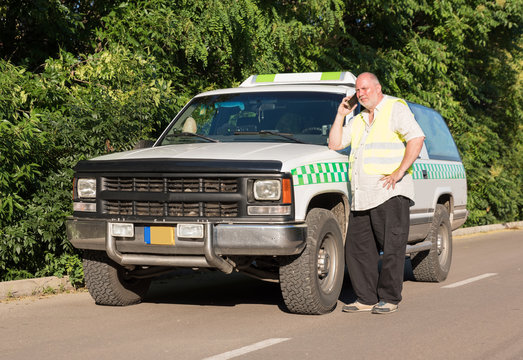 A mature man talking on his phone while standing next to his pickup truck in a sunny outdoor environment.
