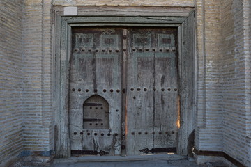 Old wooden big gate with a small door in an old brick building. Bukhara. Uzbekistan