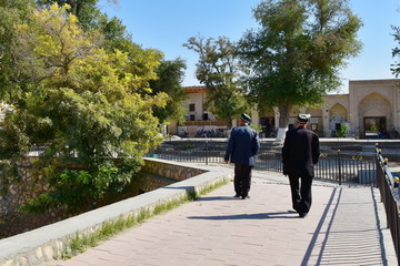 Two men in tubitejkahi jackets stroll through the old town of Bukhara. Uzbekistan.