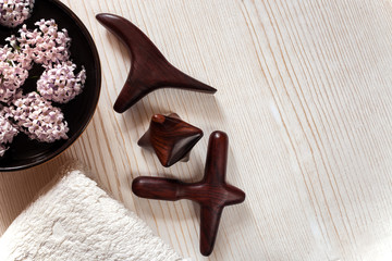 SPA and massage concept. Wooden massage sticks, terry towel, bowl with flowers on wooden background.