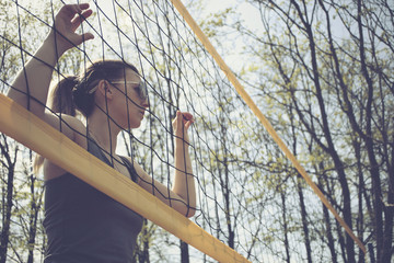 Exquisite female is standing on the beach playground next to stretched yellow volleyball net. girl in dark glasses posing near the volleyball net stands next to the volleyball net