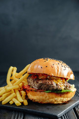 homemade  juicy burger on dark wooden board with French fries. Street food, fast food.