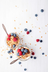 Two jars with granola, berries and yogurt on white wooden table. Top view.