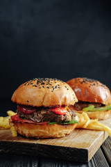 homemade juicy burgers on dark wooden board with French fries. Street food, fast food.