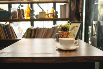 cup of coffee with plants and picture frame place on top of wooden table in living room has bookshelf background