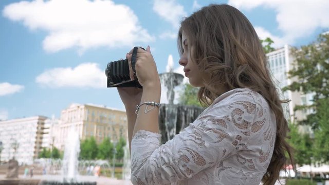 Beautiful girl takes photos of city attractions, on a vintage camera