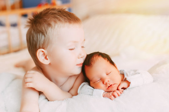 Elder brother and newborn baby sister lying on bed at home