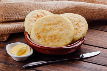 Plate with arepas and butter aside on a rustic wooden background