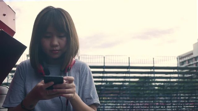 Beautiful young asian woman listening to music on a smart phone in the city. Young asian woman relaxing listening to music on the street.