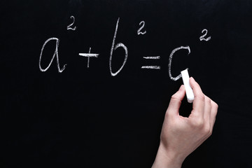 Female hand writing maths formulas on chalkboard