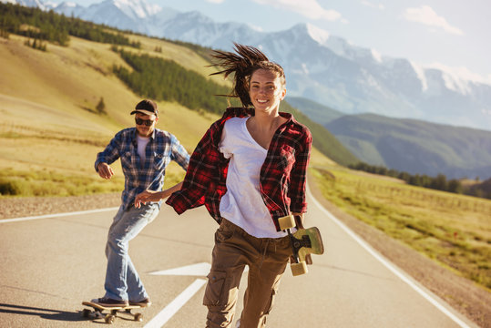 Happy friends with skates and longboards at straight road