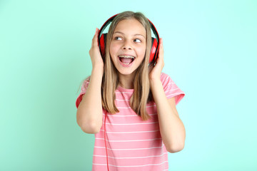 Beautiful young girl with headphones on mint background