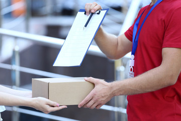 Delivery man in red uniform with cardboard box and clipboard