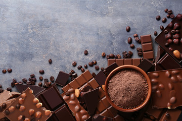 Chocolate pieces with cocoa powder in bowl and coffee beans on wooden table
