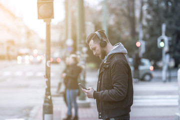 A handsome young hipster man checking his smartphone while waiting at a crosswalk.