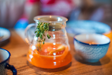 Summer tea in a large pot with a sprig. Tea with mango and orange on the table in a cafe