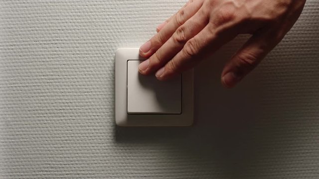 Human hand turn off a power button on a light-grey wall - Front view