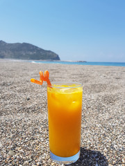 A woman hold a glass of fresh orange juice on the beach sand