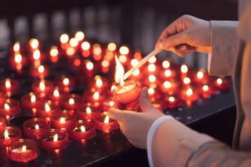 A girl is holding candle and praying near altar in church. - obrazy, fototapety, plakaty