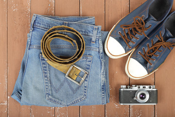 Clothes, shoes and accessories - Top view belt, gumshoes, camera  and blue jeans on wooden background